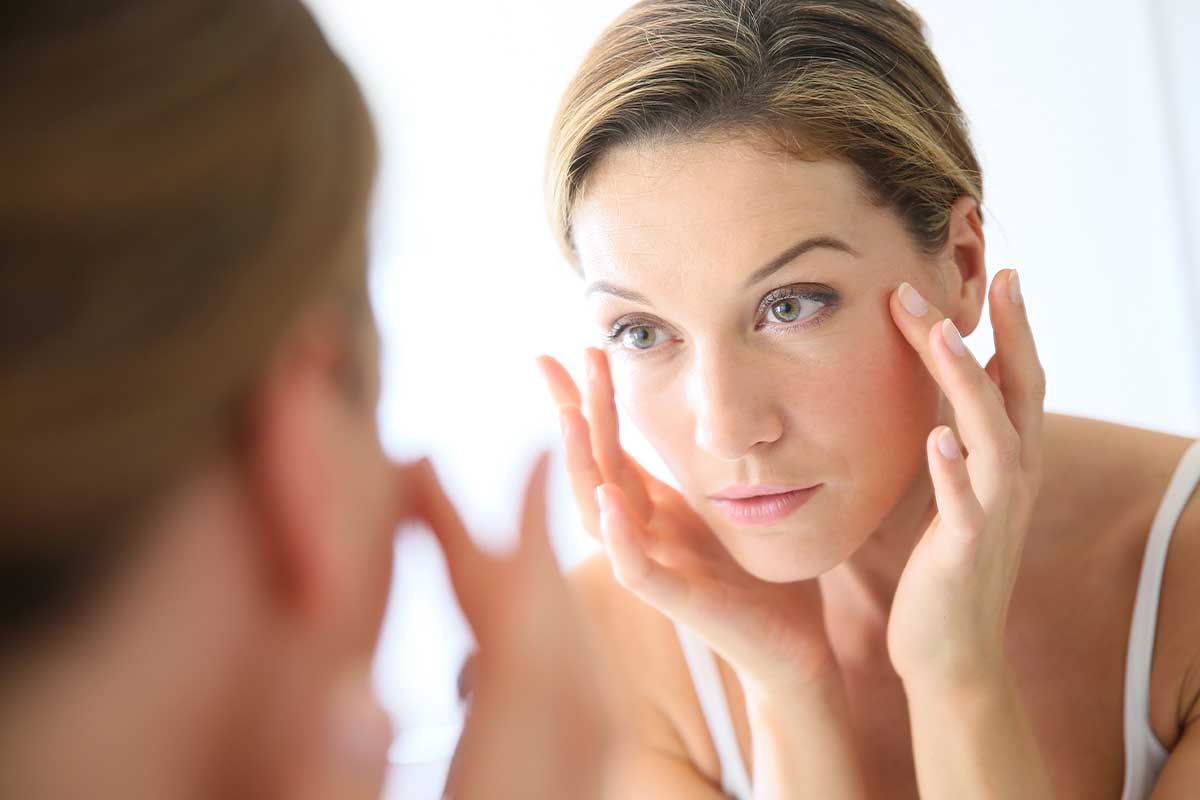 Woman examining her skin in a mirror.