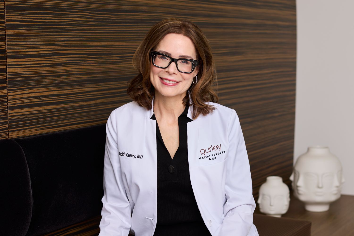 Female doctor in white coat, smiling warmly.