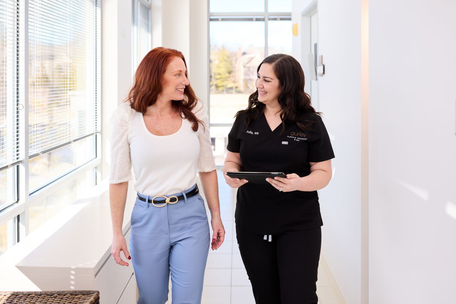 Two women talking in a bright hallway.