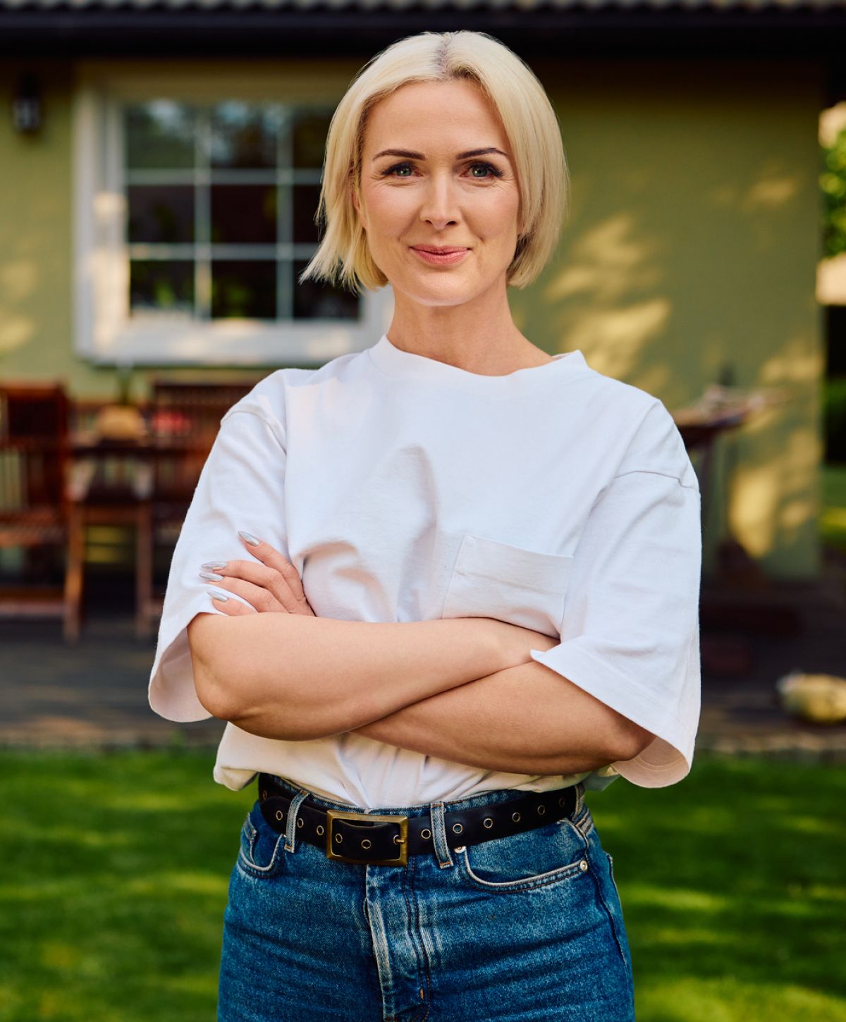 Woman smiling outdoors with arms crossed.