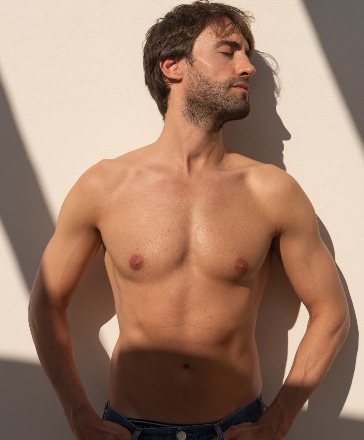 Shirtless man posing against a wall.