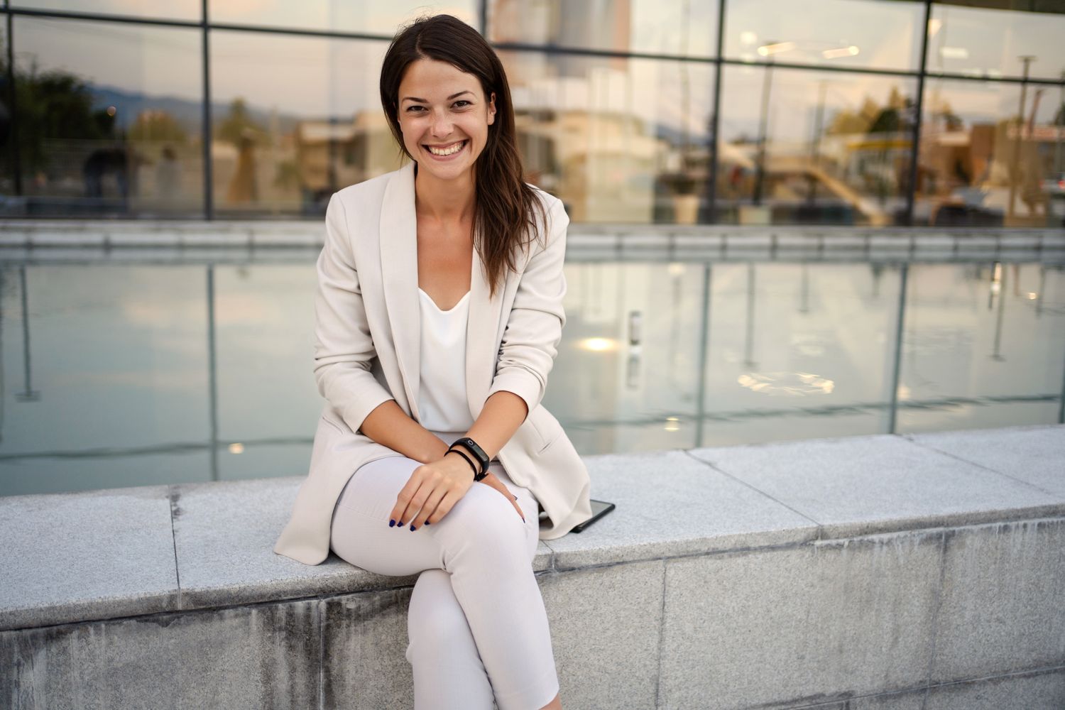 Smiling woman in light suit by water feature.