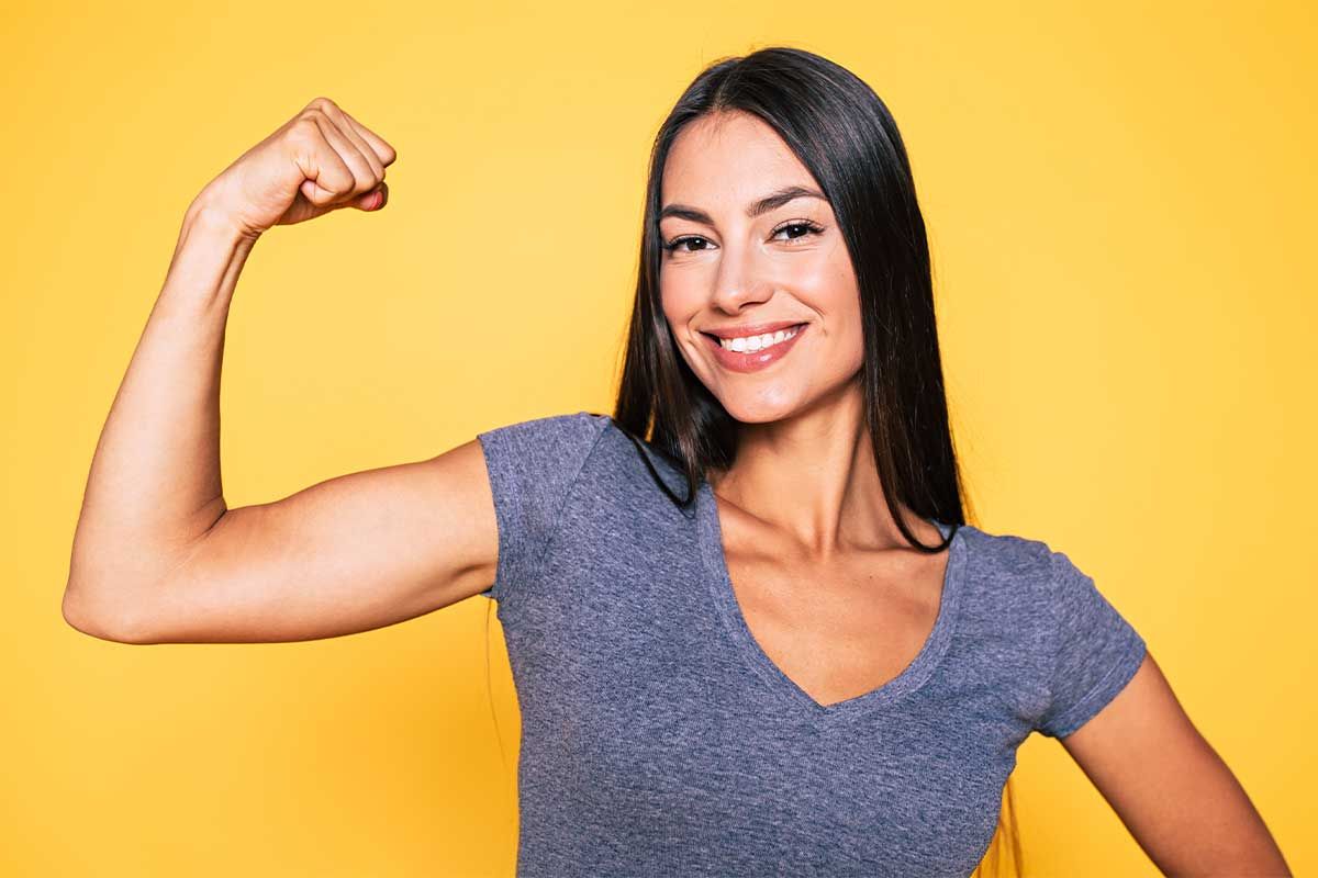 Smiling woman flexing arm against yellow background.