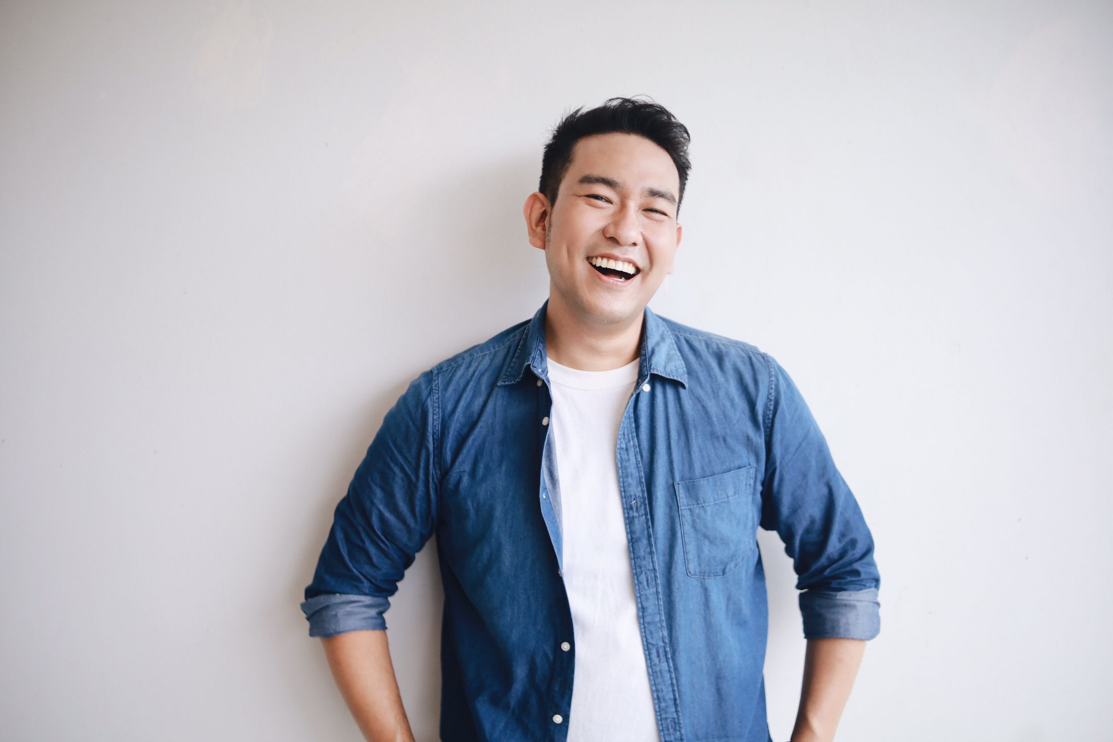 Smiling man in denim shirt against plain background.